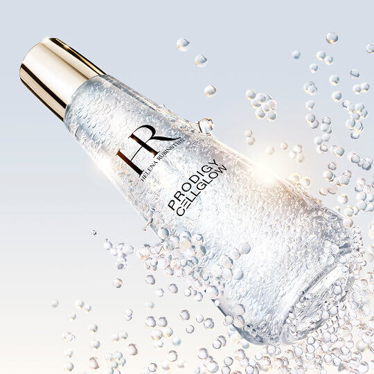 Helena Rubinstein Prodigy Cellglow serum bottle filled with bubbles, tilted and surrounded by sparkling suspended bubbles, on a bright and luminous background.