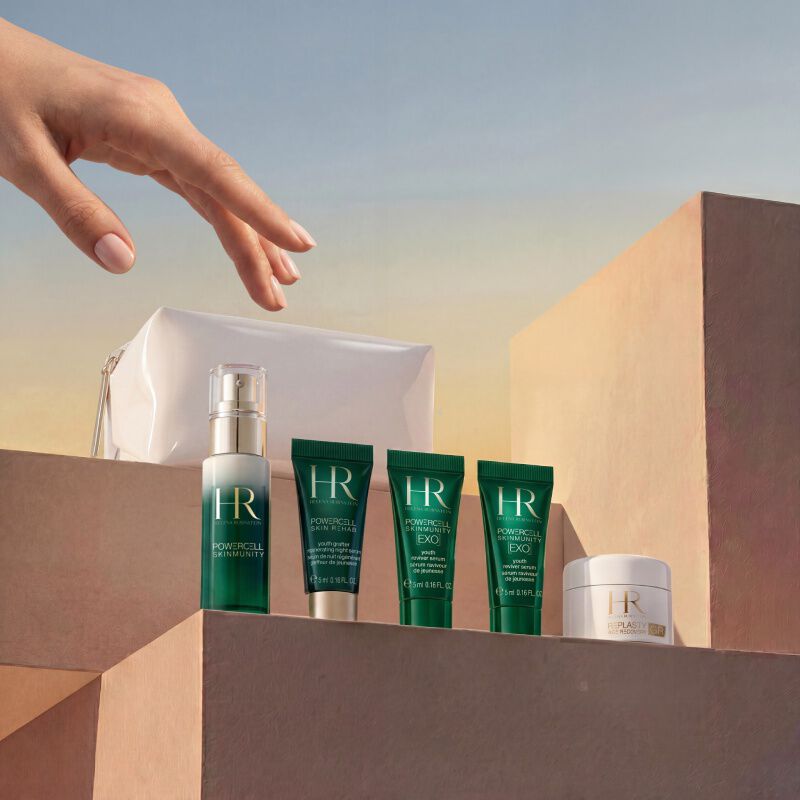 A hand reaching for a bottle of skin care products on a wooden surface.