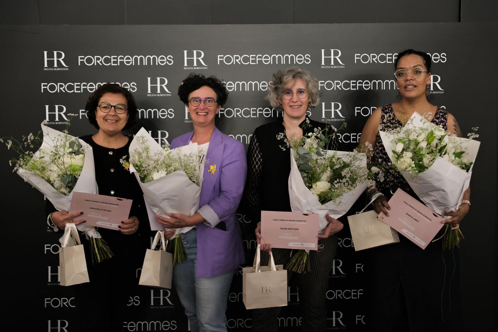 Four smiling women receive bouquets of white flowers and certificates, posing in front of a black wall featuring "HR" and "FORCEfemmes" logos.