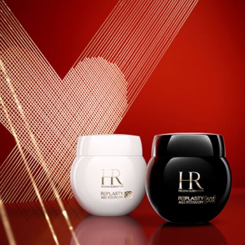 Product shot of Helena Rubinstein Re-Plasty Age Recovery Day Cream in a glossy white jar and Re-Plasty Age Recovery Night Cream in a glossy black jar. The jars sit side-by-side on a reflective red surface against a deep red background with a gold line-art heart.​