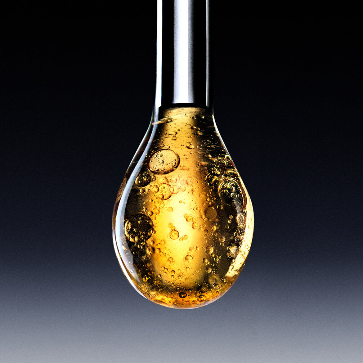 A large drop of sparkling golden liquid, like a serum or oil, about to fall from an applicator, against a dark gradient background.