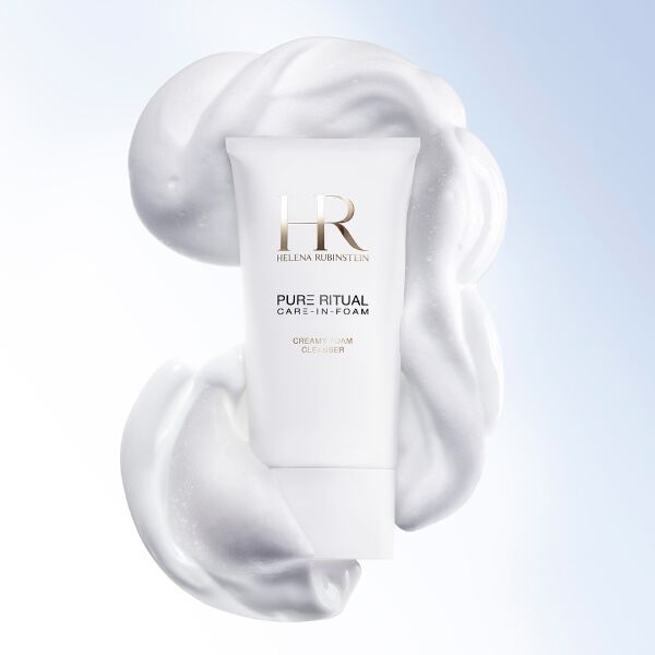 Close-up of the Helena Rubinstein Pure Ritual Care-in-Foam cleanser surrounded by creamy white foam, next to the face of a woman with a pure and luminous complexion.​