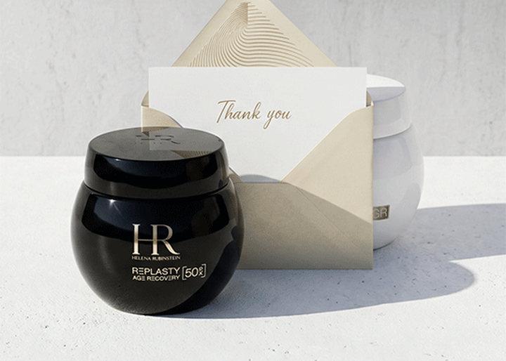 A black jar of Helena Rubinstein Replanty Age Recovery cream and an envelope with a "Thank you" card sitting on a white surface, with a white jar in the background.