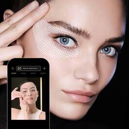 A close-up of a model with striking blue eyes, showcasing beauty tech on a smartphone screen beside her.