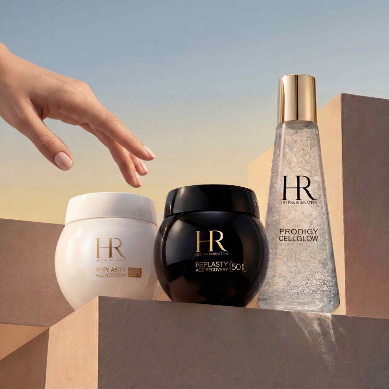 Helena Rubinstein's Prodigy Cellglow serum bottle (clear, bubbles) and Re-Plasty cream jar (black). Placed on a textured and luminous white background, symbolizing elegance and skincare effectiveness.