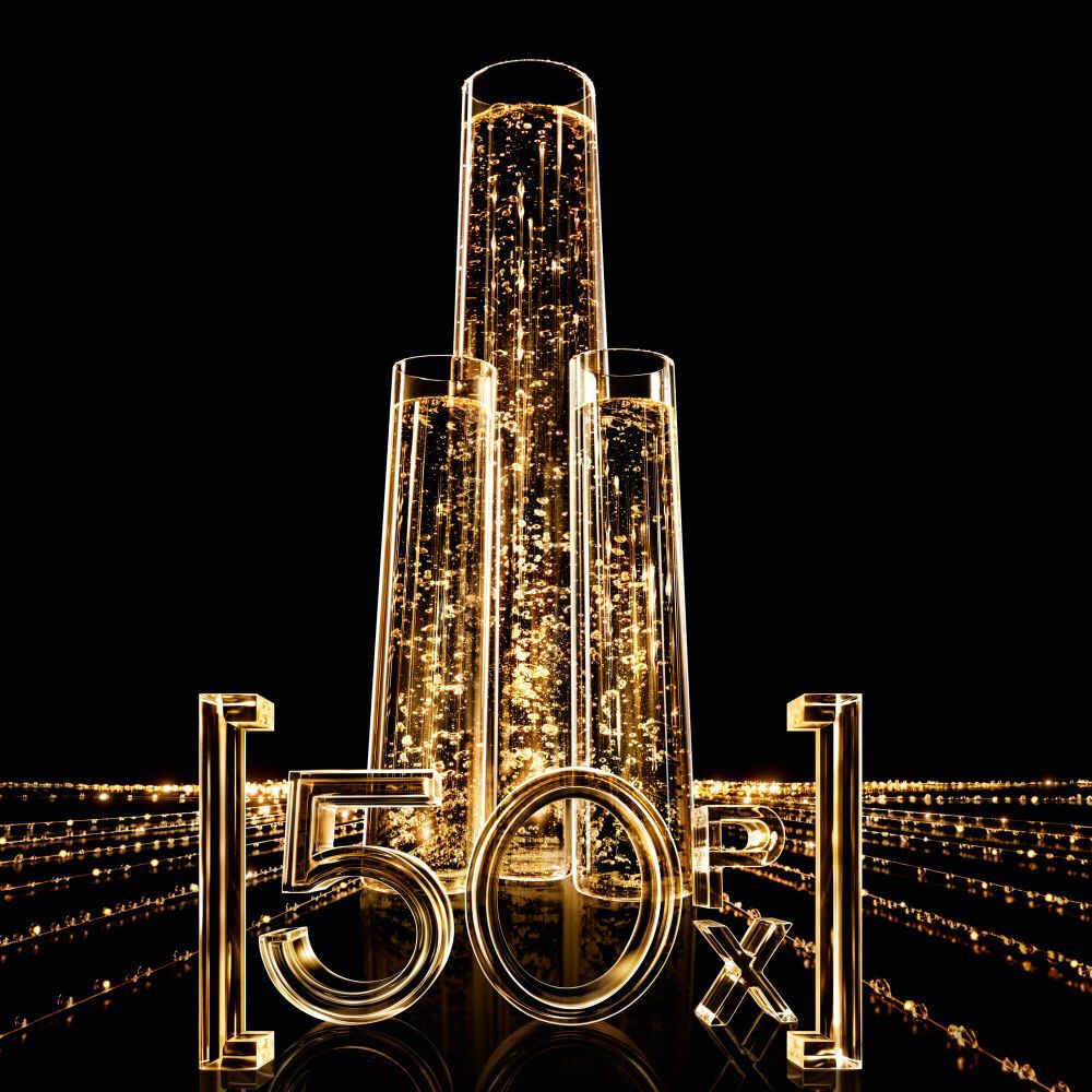 Three vertical glass tubes filled with sparkling golden liquid, with luminous "50X" numbers in front, on a black background with golden light trails.
