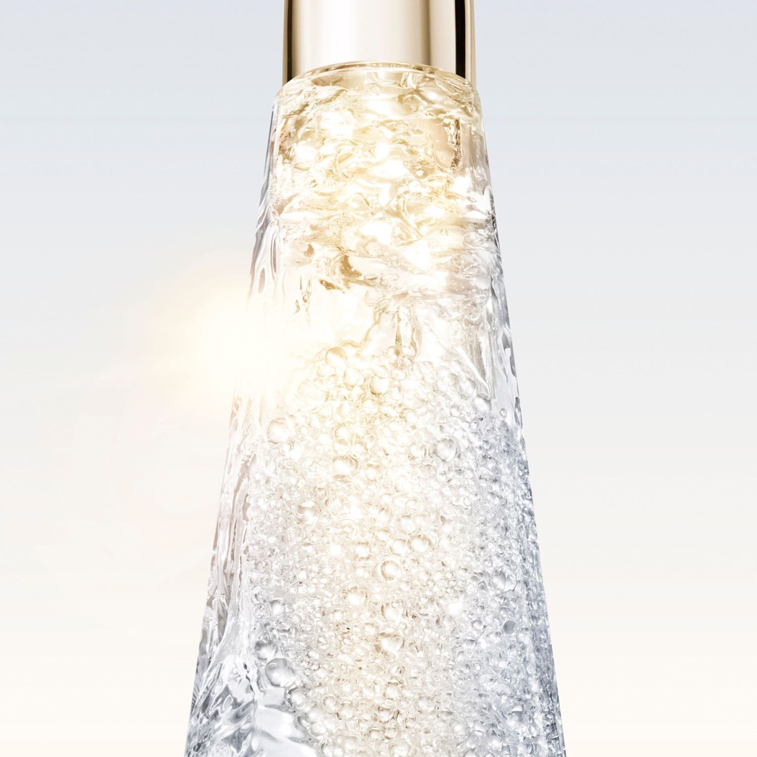 Vertical close-up of a transparent serum bottle, filled with hydrating beads, featuring a bright glow at the center and a golden cap. The gel texture is visible.