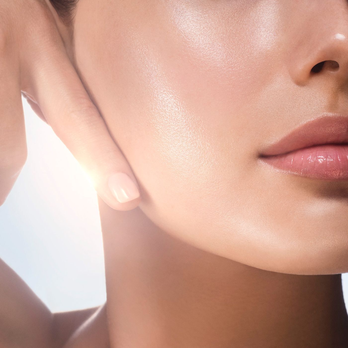 Bright close-up of a woman's healthy, glowing skin, with a hand gently touching the cheek. The light highlights the hydrated complexion and rosy lips.