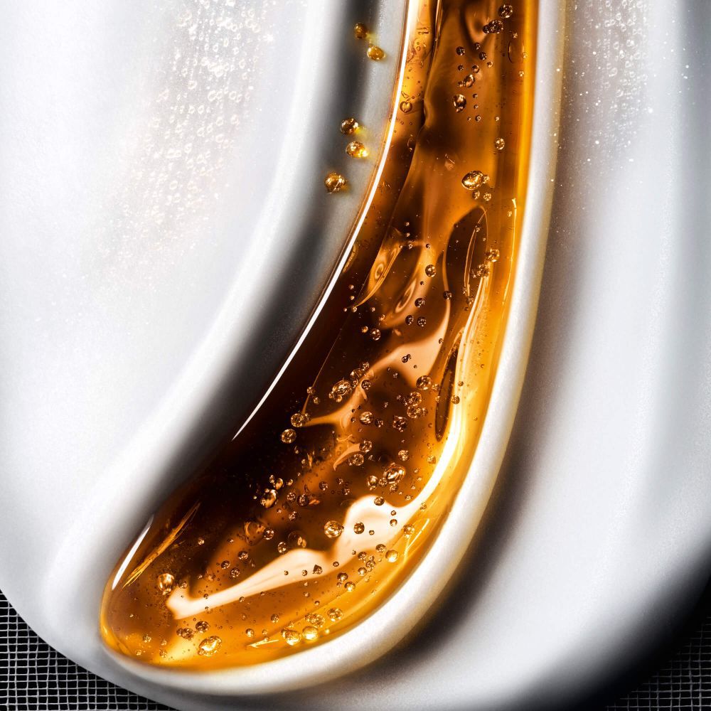 Close-up of a fluid cosmetic texture, blending waves of shimmering golden gel with bubbles on a creamy white background, evoking rich skincare.