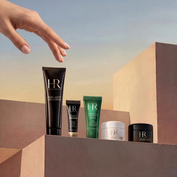 A hand reaching for a bottle of skin care products on a wooden surface.